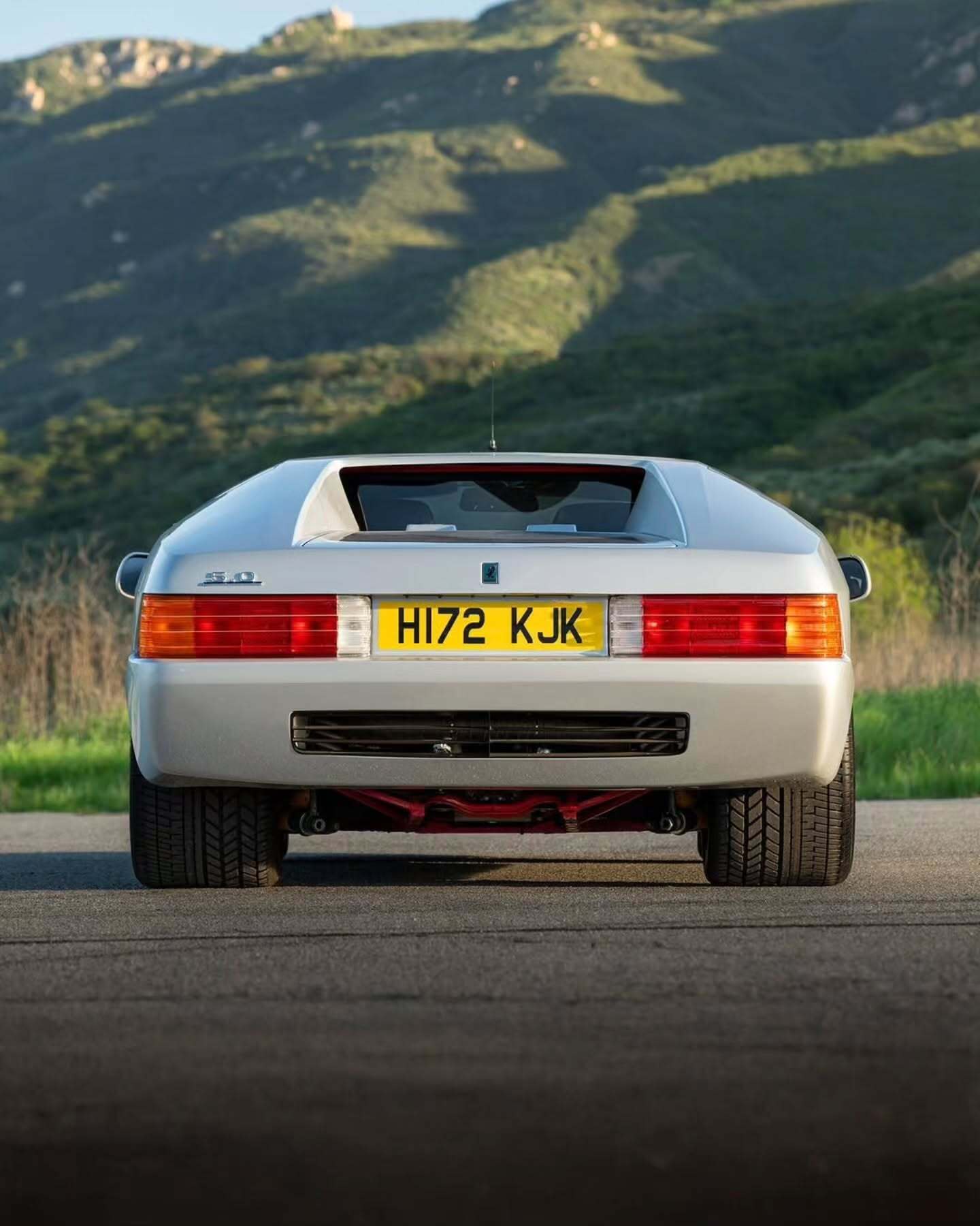 نمای جانبی ابرخودروی کلاسیک ایزدرا امپراتور 108i با رنگ نقره‌ای، آینه پیروسکوپی روی سقف و درهای بال‌کبوتری در یک فضای نمایشگاهی.